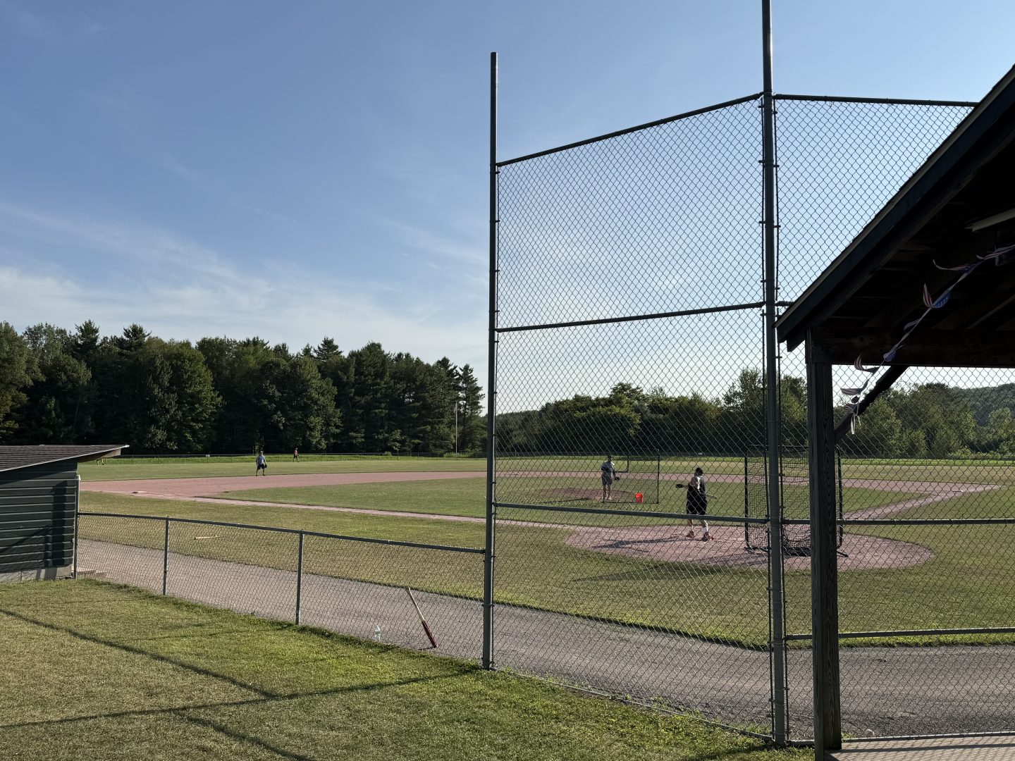 Baseball field with players practicing, sunny weather, and a clear sky.