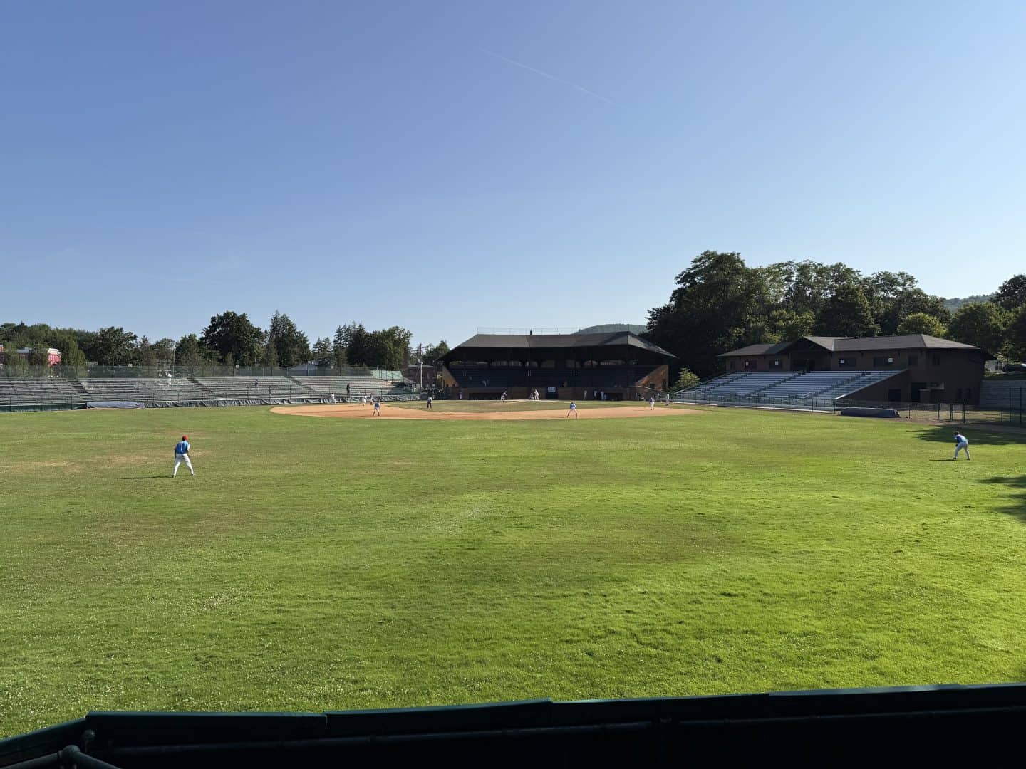 Baseball players practicing on a lush green field under a clear blue sky.