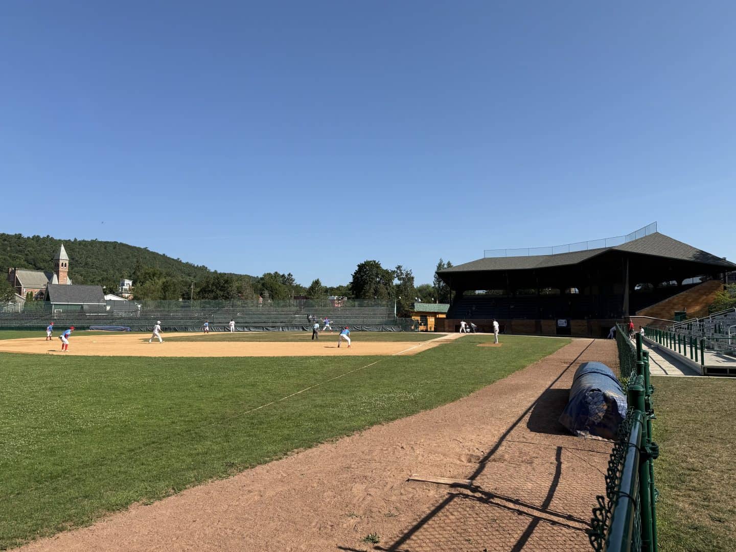 Outdoor baseball field with players practicing under clear blue skies.